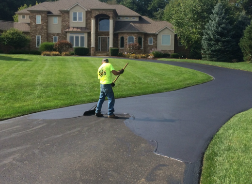 Wide view of crew member sealcoating driveway at large residential property